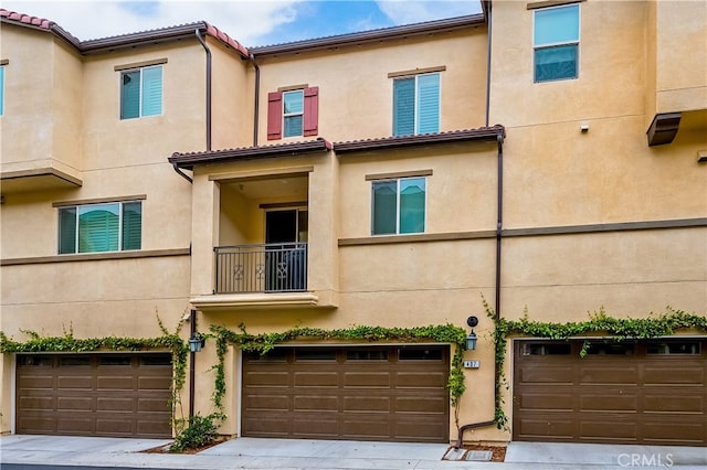 view of property with an attached garage, a balcony, and stucco siding