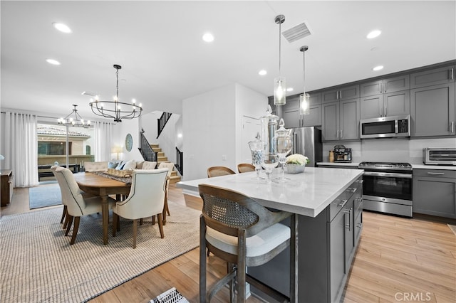 kitchen with a center island, a notable chandelier, gray cabinets, light wood-style flooring, and appliances with stainless steel finishes