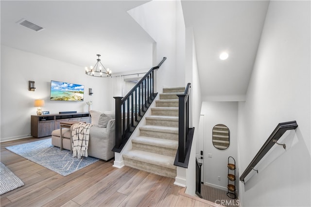 stairway featuring wood finished floors, visible vents, baseboards, and an inviting chandelier