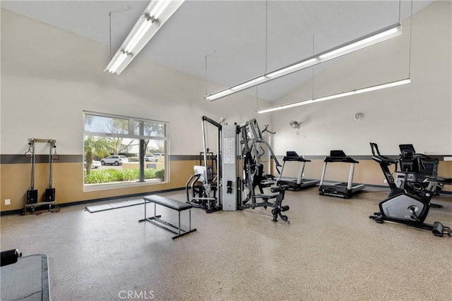 exercise room with baseboards and a towering ceiling
