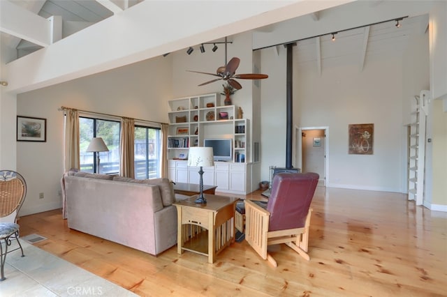 living room featuring light wood-style floors, beamed ceiling, ceiling fan, high vaulted ceiling, and a wood stove