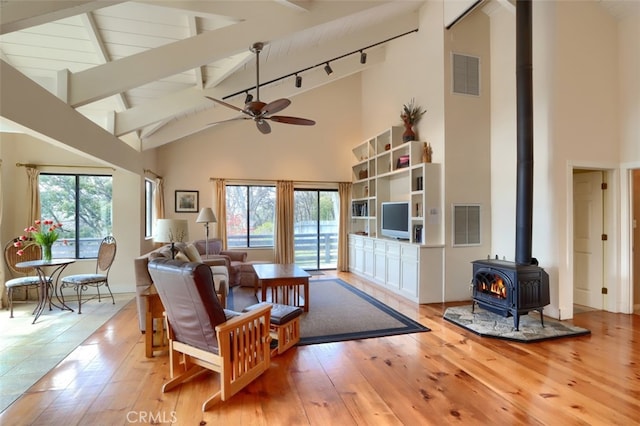 living room featuring high vaulted ceiling, light wood finished floors, a wood stove, and visible vents