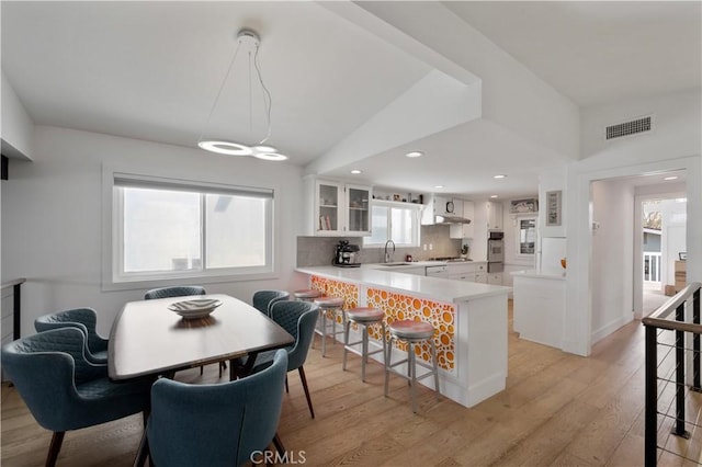 kitchen featuring glass insert cabinets, white cabinets, visible vents, a sink, and a peninsula