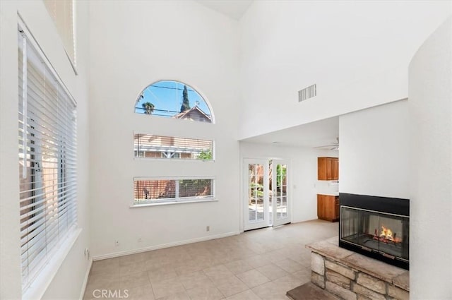 living area featuring a multi sided fireplace, a healthy amount of sunlight, a high ceiling, and visible vents