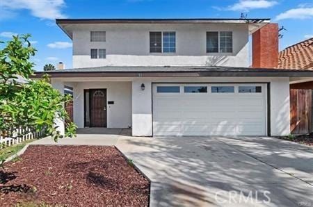 traditional-style house with an attached garage, a chimney, fence, stucco siding, and driveway