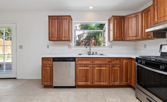 kitchen featuring under cabinet range hood, light countertops, a sink, stainless steel appliances, and brown cabinets