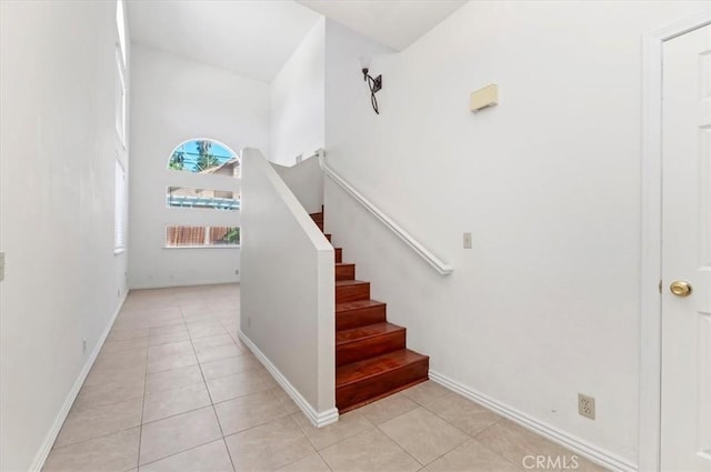 stairs with baseboards, tile patterned flooring, and a towering ceiling