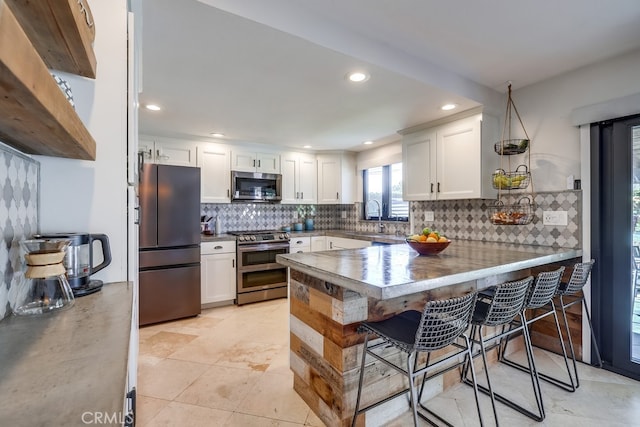 kitchen with decorative backsplash, a peninsula, appliances with stainless steel finishes, a breakfast bar area, and white cabinetry