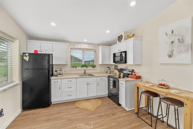 kitchen with white cabinets, a sink, light countertops, light wood-type flooring, and black appliances