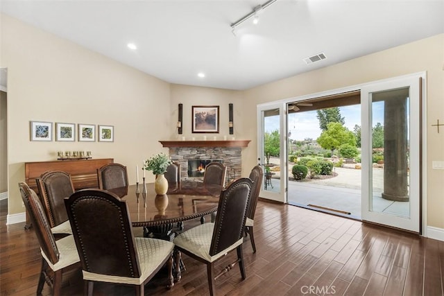 dining area featuring baseboards, a stone fireplace, track lighting, dark wood-type flooring, and visible vents