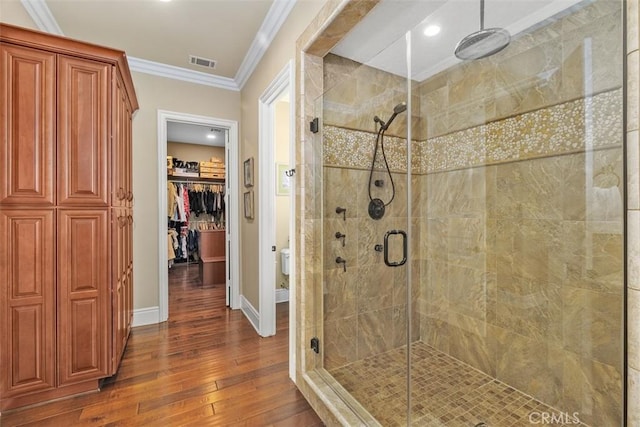 full bathroom with ornamental molding, toilet, a shower stall, visible vents, and hardwood / wood-style floors