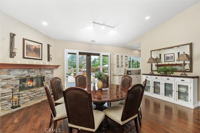 dining area featuring track lighting, a fireplace, visible vents, hardwood / wood-style floors, and lofted ceiling