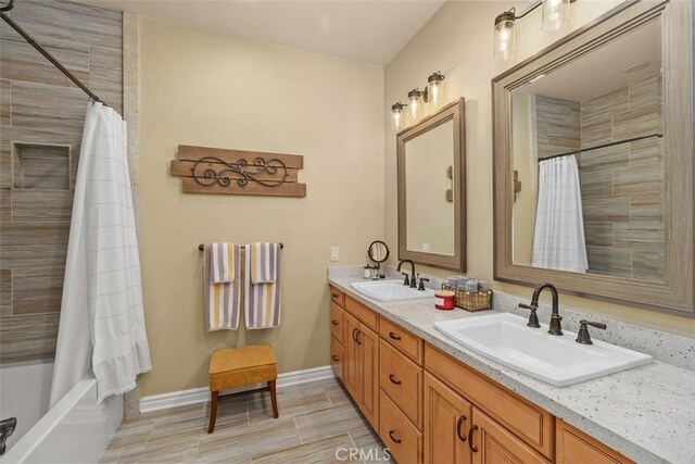 full bathroom with shower / bath combination with curtain, double vanity, a sink, and baseboards