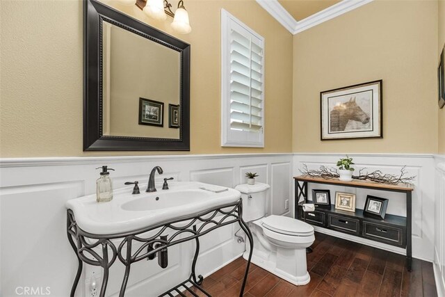 half bath featuring a decorative wall, ornamental molding, a wainscoted wall, toilet, and wood finished floors