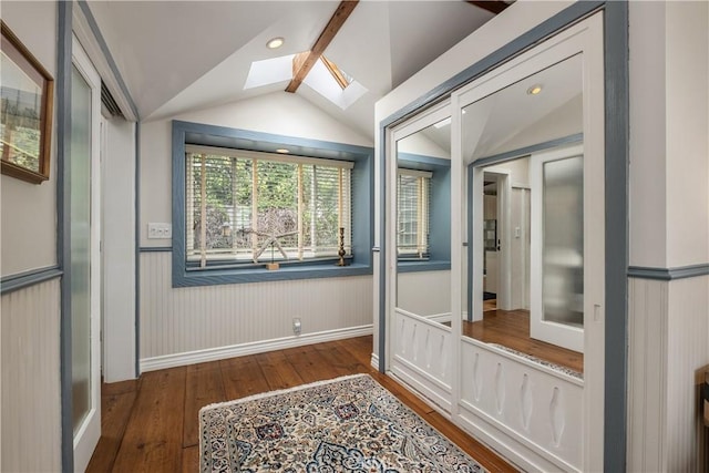 hall with hardwood / wood-style flooring, vaulted ceiling with skylight, and a wainscoted wall