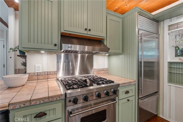 kitchen featuring extractor fan, tile counters, premium appliances, and green cabinetry