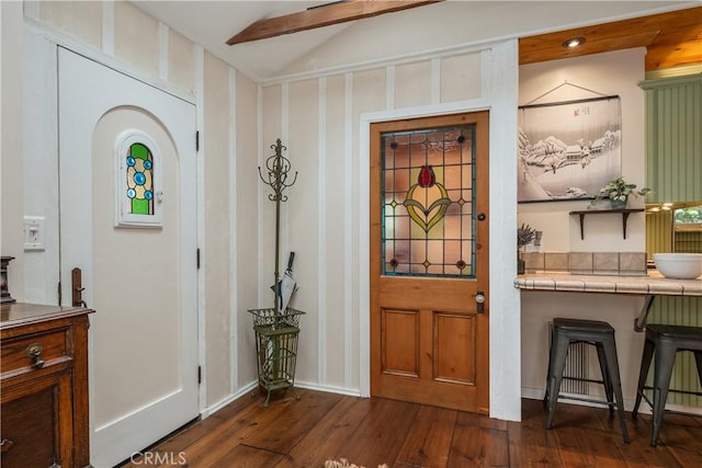 entryway with dark wood-type flooring and vaulted ceiling with beams