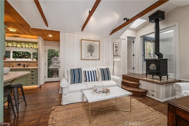 living area with a wealth of natural light, a wood stove, vaulted ceiling with beams, and dark wood-style floors