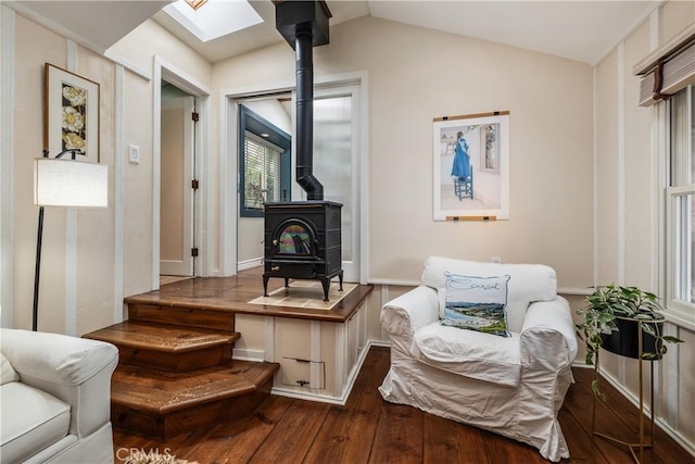 sitting room featuring vaulted ceiling with skylight, a wood stove, and hardwood / wood-style flooring
