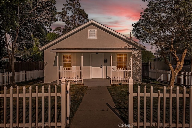 bungalow-style house featuring a fenced front yard, a yard, covered porch, and stucco siding