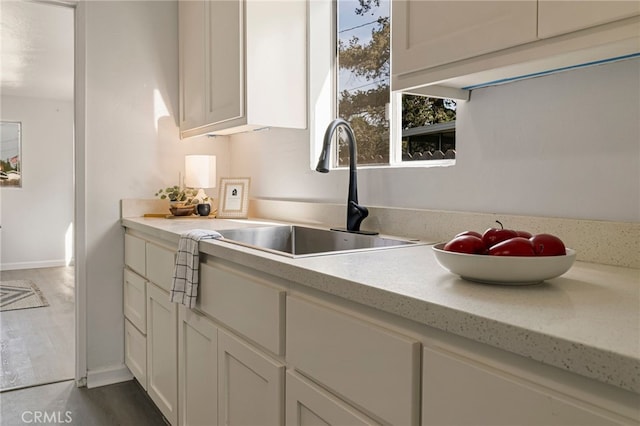 kitchen with a sink, light countertops, baseboards, and dark wood-style flooring