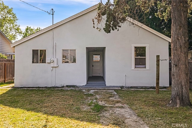 view of front of home featuring stucco siding, fence, and a front lawn