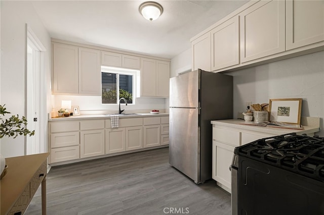 kitchen featuring a sink, light countertops, freestanding refrigerator, range with gas stovetop, and light wood finished floors