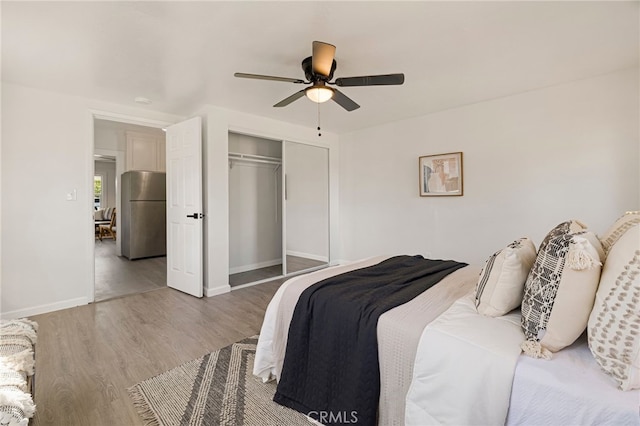 bedroom with baseboards, a closet, freestanding refrigerator, ceiling fan, and wood finished floors