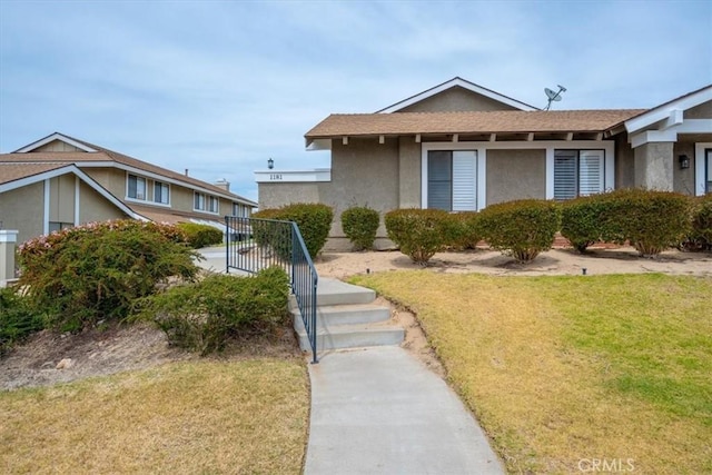 view of front of house featuring a shingled roof, stucco siding, and a front lawn