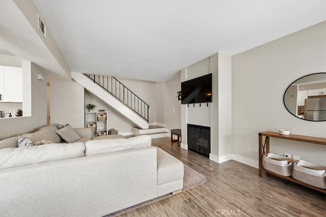 living room featuring baseboards, a fireplace, light wood-style flooring, stairs, and visible vents
