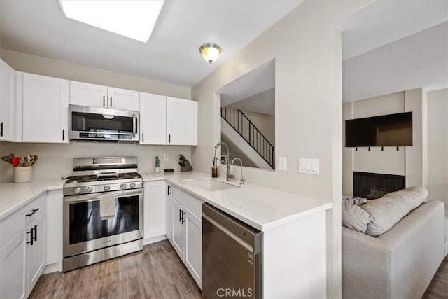 kitchen featuring white cabinets, a sink, light countertops, light wood-type flooring, and appliances with stainless steel finishes