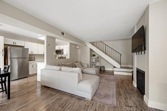 living area featuring wood finished floors, baseboards, visible vents, and stairs