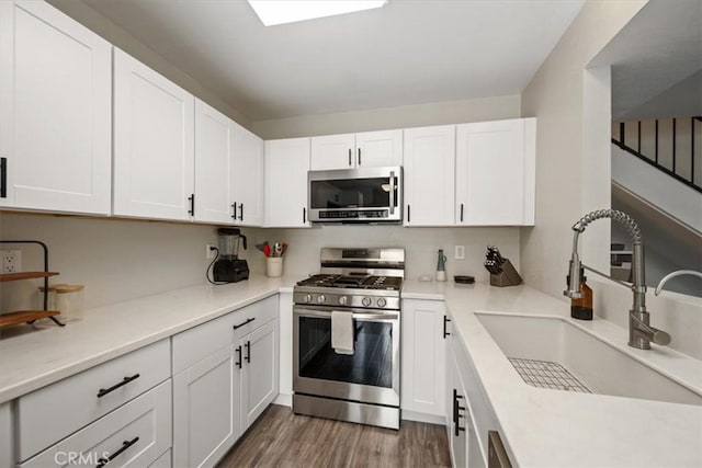 kitchen with white cabinetry, wood finished floors, light countertops, a sink, and stainless steel appliances