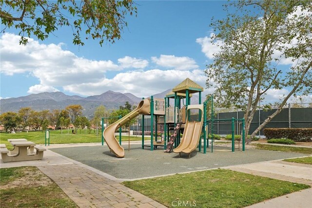 community playground featuring a mountain view, fence, and a lawn