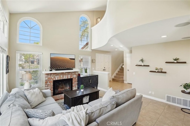 living area with visible vents, stairway, a towering ceiling, and a brick fireplace