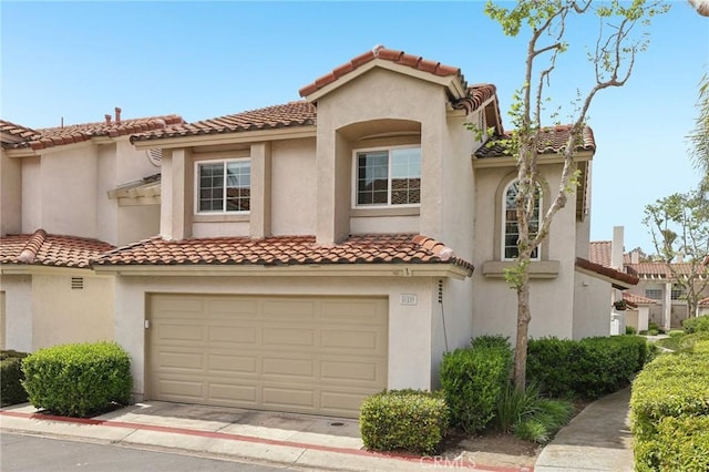 mediterranean / spanish-style house with driveway, stucco siding, a tiled roof, and an attached garage