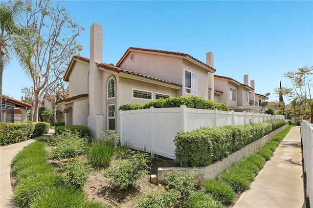 view of home's exterior with a tiled roof, fence, stucco siding, and a chimney