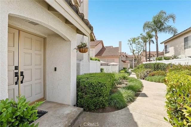 entrance to property featuring fence, a residential view, and stucco siding