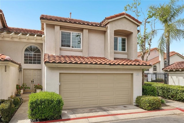 mediterranean / spanish-style home with a tiled roof, stucco siding, fence, an attached garage, and driveway