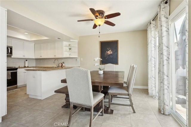 dining room featuring a tray ceiling, light tile patterned flooring, baseboards, and a ceiling fan