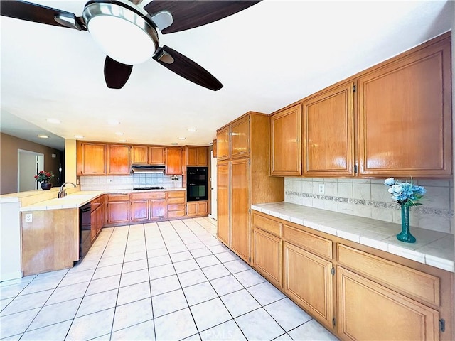 17346 Cold Spring Cir, Riverside, CA 92503 - kitchen with under cabinet range hood, light tile patterned floors, tasteful backsplash, black appliances, and a peninsula