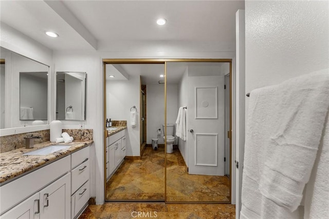 bathroom featuring two vanities, recessed lighting, toilet, stone finish flooring, and a sink