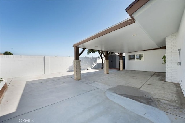 view of patio / terrace featuring a shed, a carport, a fenced backyard, and an outdoor structure