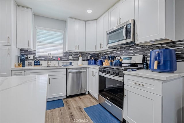 kitchen featuring light wood-style flooring, tasteful backsplash, white cabinets, a sink, and stainless steel appliances