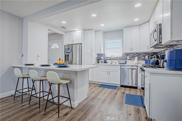 kitchen featuring light wood-style floors, a peninsula, a breakfast bar, appliances with stainless steel finishes, and decorative backsplash