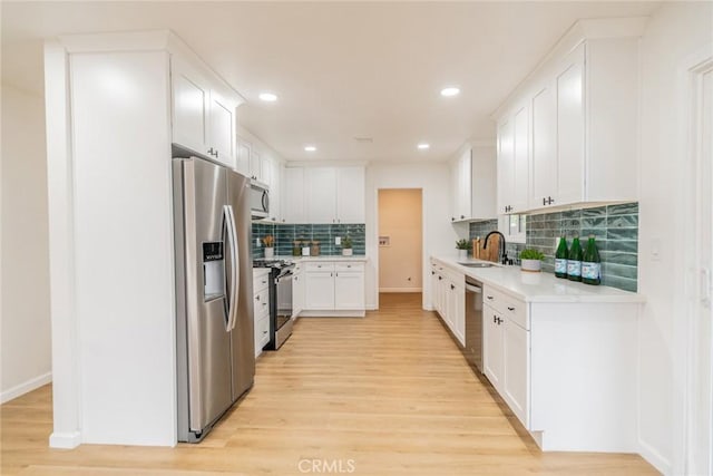 kitchen with decorative backsplash, light wood-style flooring, stainless steel appliances, light countertops, and white cabinetry