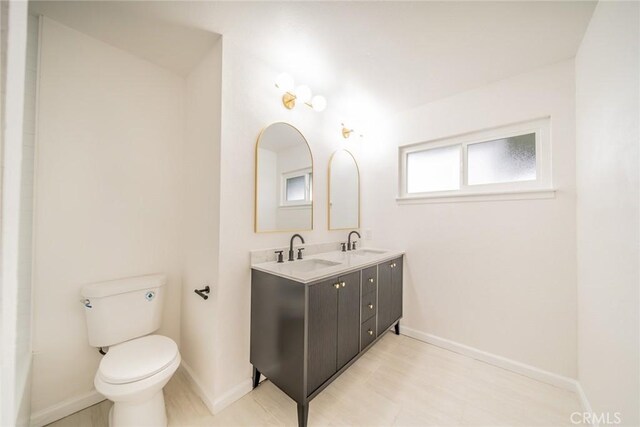 full bath with baseboards, a sink, double vanity, and toilet