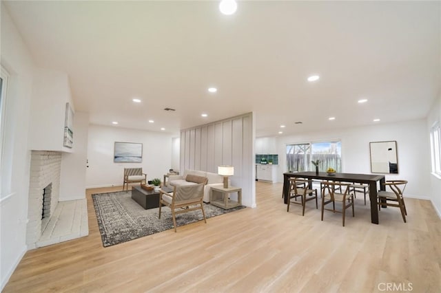 living room featuring a brick fireplace, baseboards, recessed lighting, and light wood-style floors