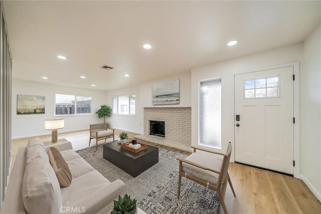 living room with a brick fireplace, recessed lighting, and light wood-style floors