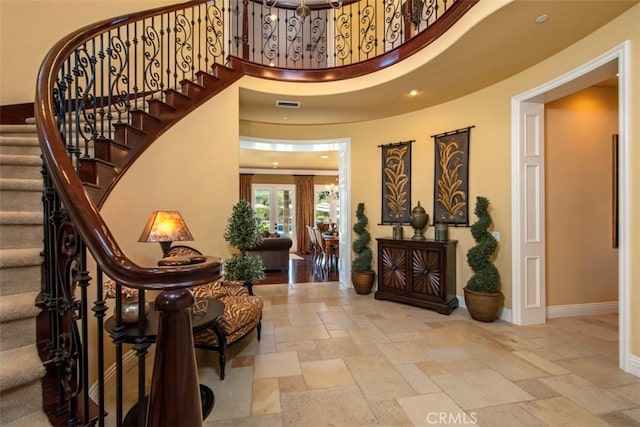 entryway featuring stone tile flooring, stairs, visible vents, baseboards, and a towering ceiling